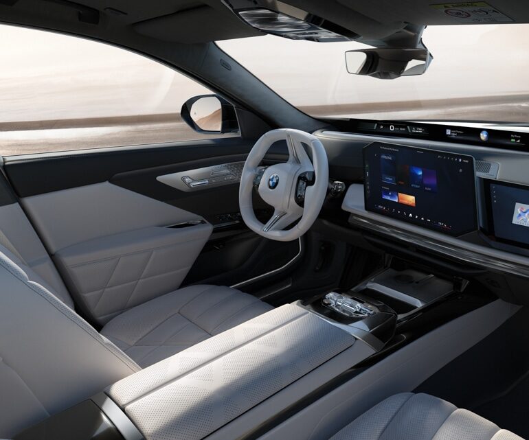 Der Innenraum eines modernen BMW 7er Fahrzeugs mit weißem Lederlenkrad, zwei großen digitalen Bildschirmen und hellen Ledersitzen mit Steppmustern. Das Armaturenbrett und die Bedienelemente haben ein schlichtes, minimalistisches Design.