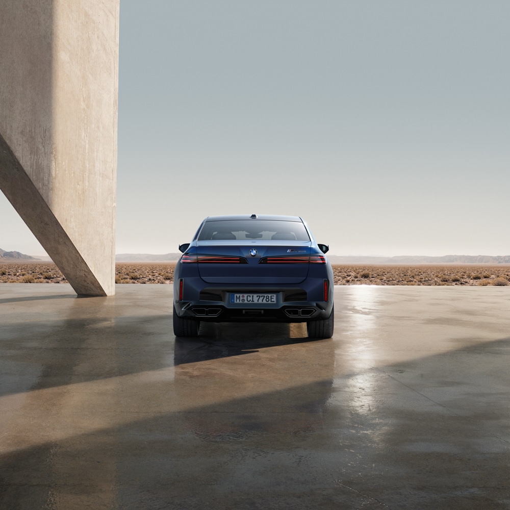 Ein blaues Auto ist auf einer polierten Betonfläche neben einem hohen Gebäude geparkt und blickt auf eine karge, wüstenartige Landschaft unter einem klaren Himmel. Die Szene ist minimalistisch und hat eine moderne, geometrische Anmutung.