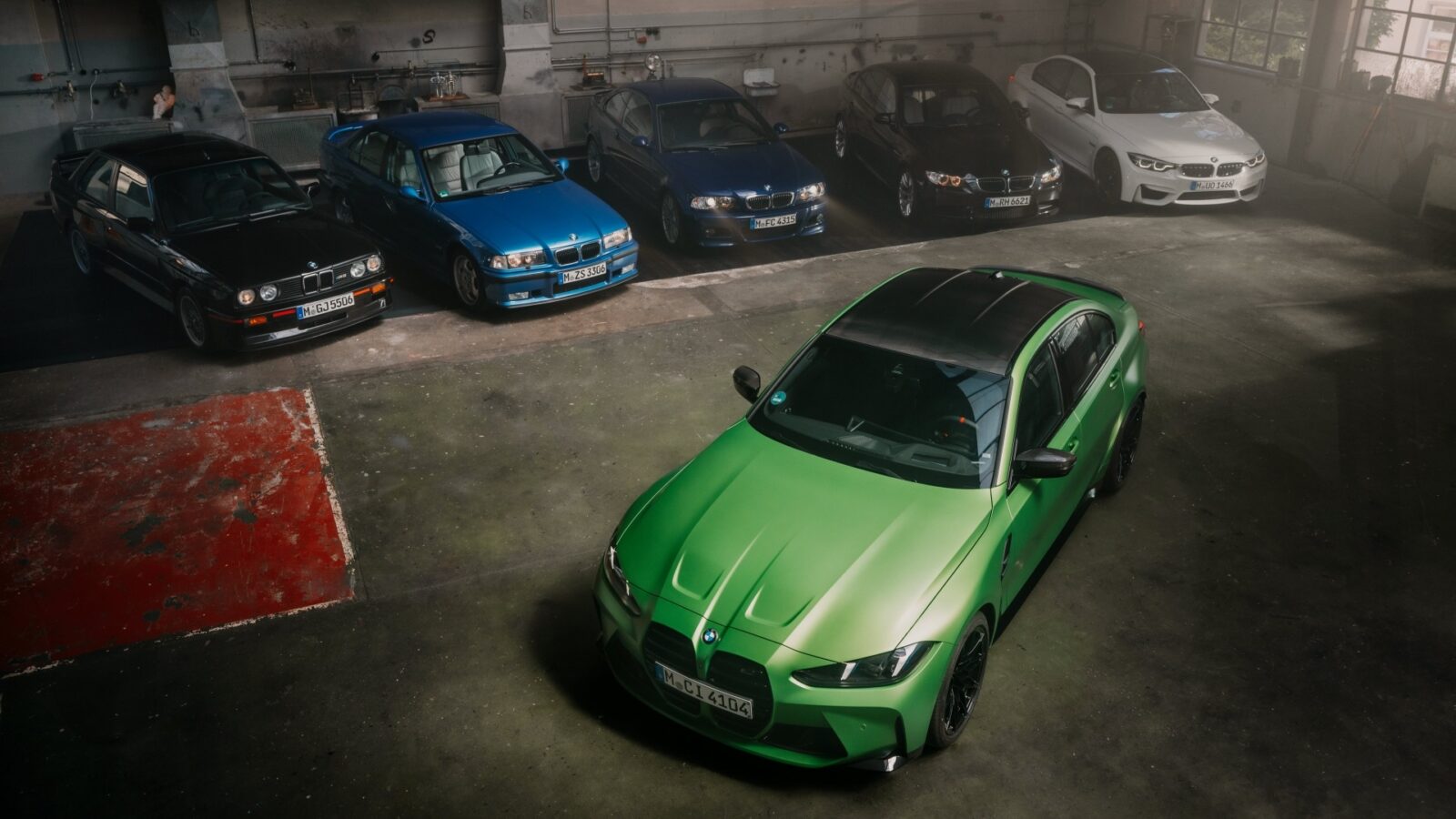 Sechs BMW M3 aus verschiedenen Generationen sind in einer geräumigen Garage geparkt. Fünf Autos in verschiedenen Farben sind im hinteren Bereich in einer Reihe geparkt, während ein leuchtend grüner M3 separat im Vordergrund positioniert ist.