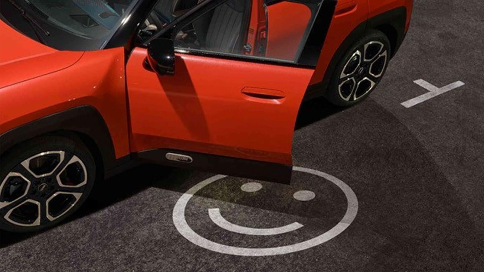 Ein roter MINI mit geöffneter Fahrertür ist über einem weißen Smiley-Symbol auf einem asphaltierten Parkplatz geparkt, das das Symbol teilweise verdeckt. Das linke Vorderrad ist nach außen gedreht.